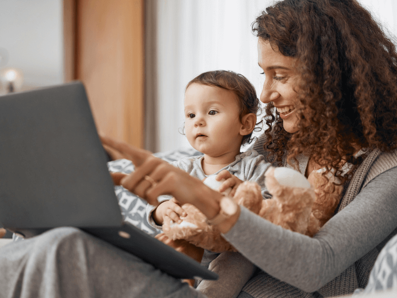 Foto de um bebê e uma mãe sentados em um sofá e olhando para um computador
