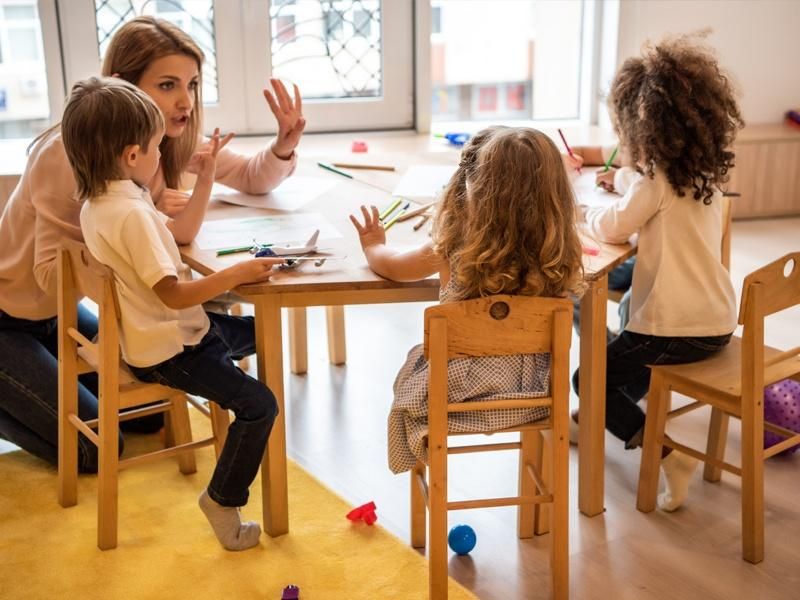 Professora branca reunida com três crianças em uma sala de aula infantil