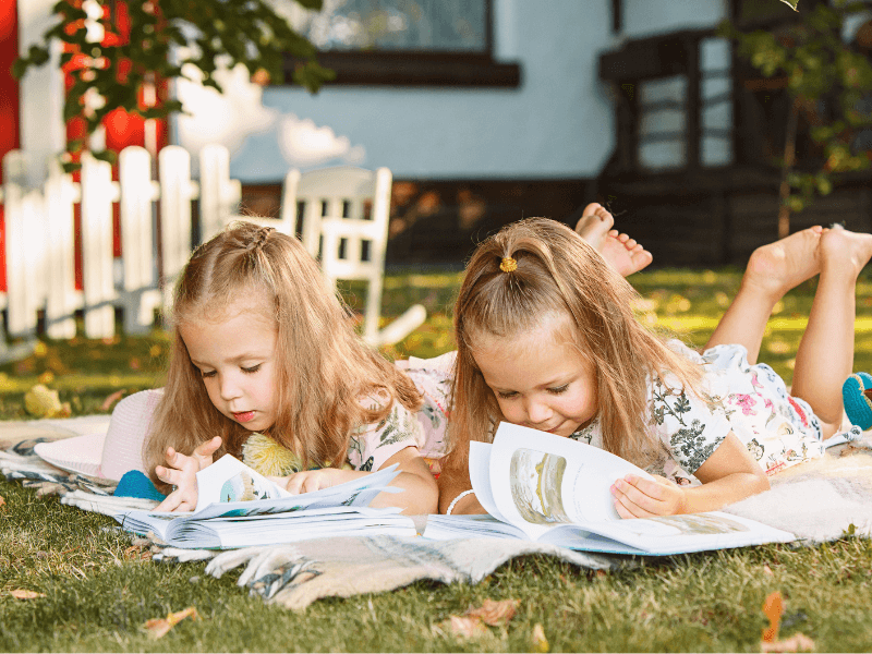Duas meninas em uma escola lendo livros deitadas sobre a grama