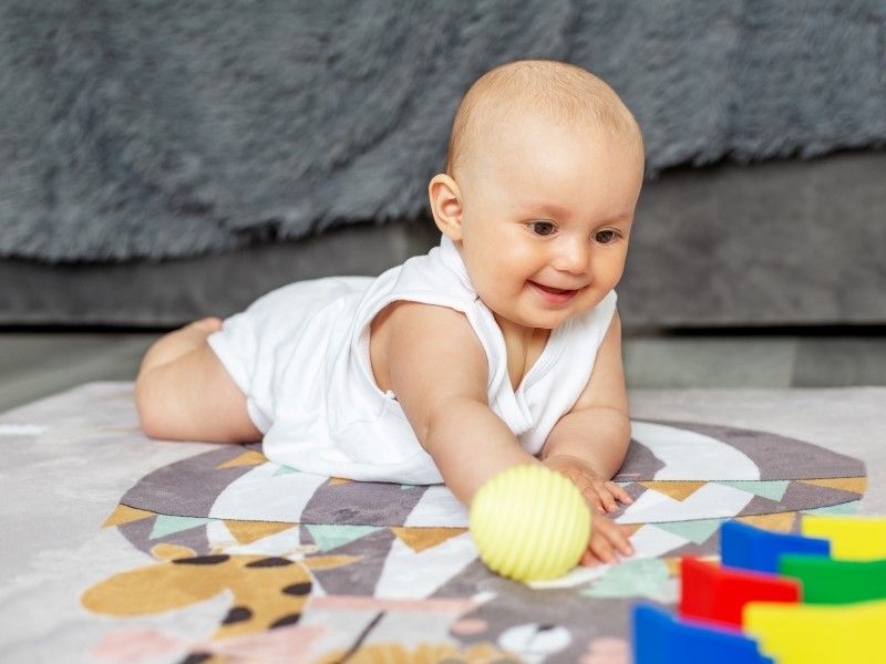 Bebê brincando com uma bolinha amarela em cima de um tapete