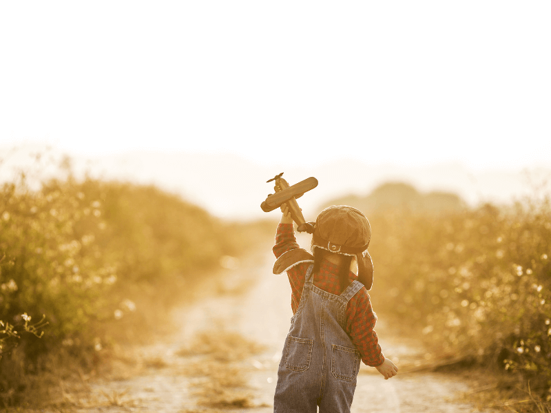 Criança segurando um avião de brinquedo em frente ao por do sol