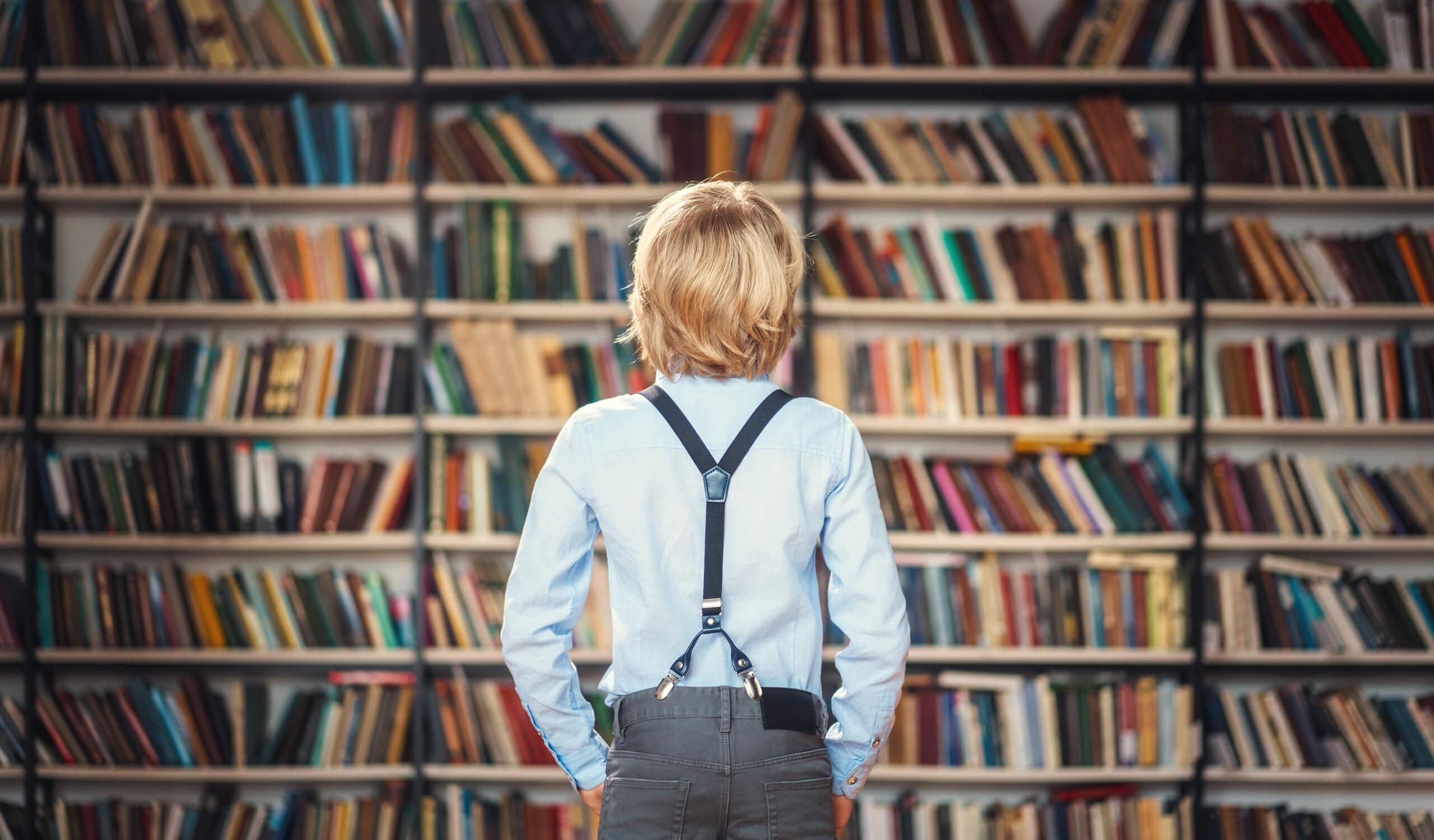 Menino loiro de costas observando estantes de livros