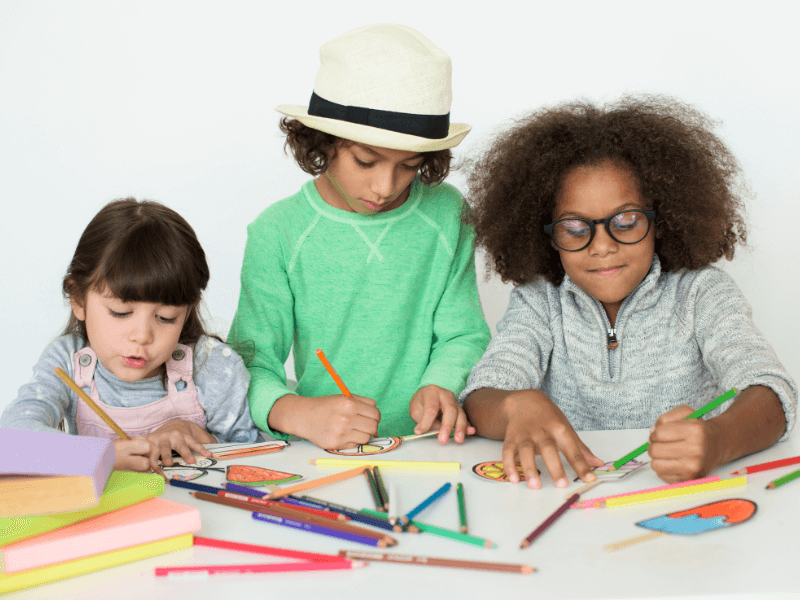 Três crianças desenhando e colorindo em folhas de papel com lápis de cor