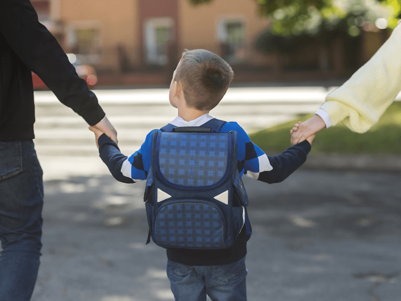 Criança branca indo para a escola e segurando as mãos de seus pais