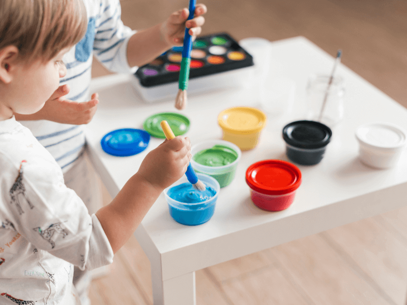 Bebê pintando um papel com um pinçel e potes de tinta